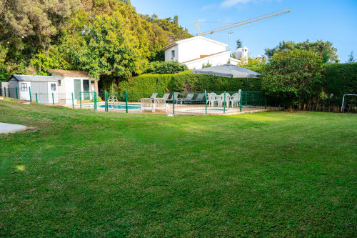 Piscina y jardines de Guest Homes Málaga con edificios blancos rodeados de árboles frondosos y cielo despejado