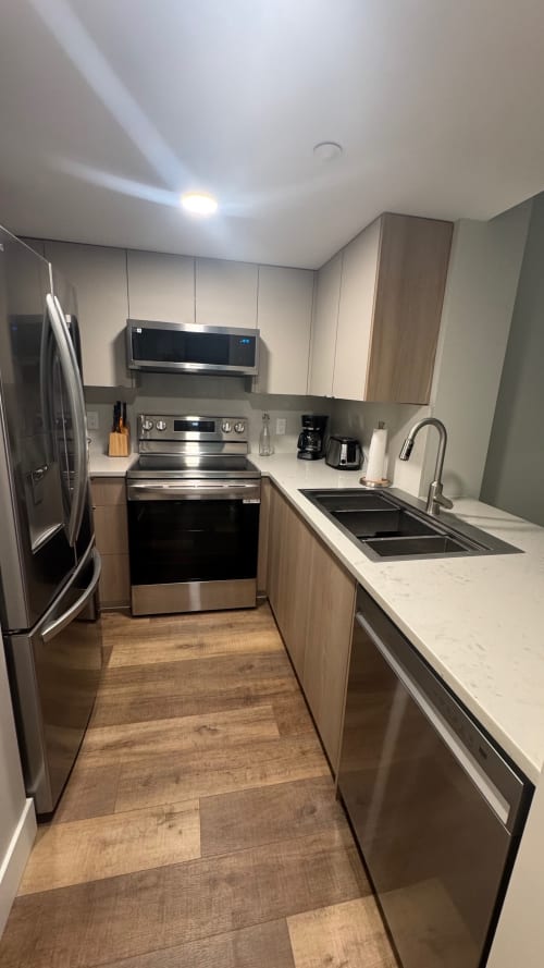 Modern kitchen in Whistler apartment with stainless steel appliances, white quartz counters, and wood cabinetry
