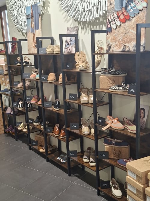 Shoe boutique display with black shelving units featuring leather sandals and shoes priced 40€-65€ at Hotel-Boutique by