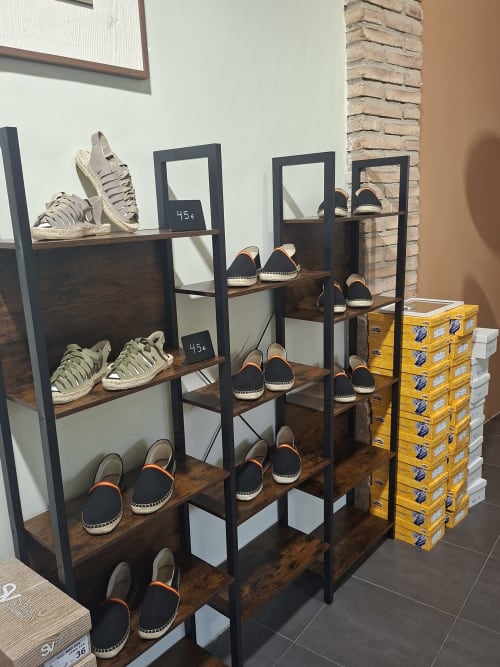 Boutique hotel shoe display with wooden shelves showing espadrilles and black canvas shoes, yellow boxes nearby in Cervera