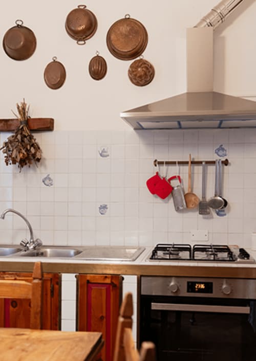 Cristallo Apartment kitchen in Ravenna with copper cookware, white tiles, gas stove, and vintage wood cabinets