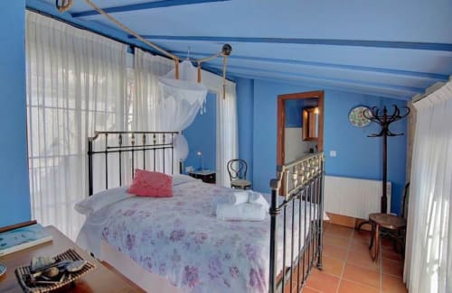 Dormitorio azul brillante en Casa Gallinera con cama de hierro forjado, dosel de gasa blanca y suelos de terracota en Benissivà, España