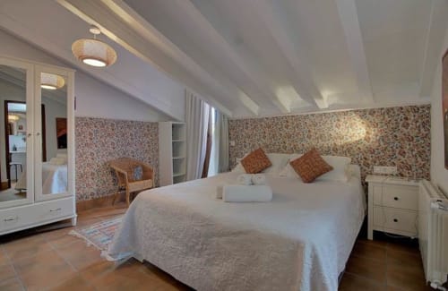 Amplio dormitorio abuhardillado en el hotel Casa Gallinera en Benissivà con papel pintado floral, ropa de cama blanca y vigas de madera