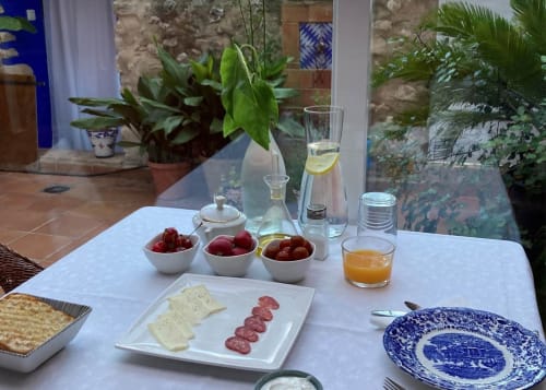 Breakfast table at Casa Gallinera Benissivà with fresh fruits, cheese, cured meats, and beverages in Mediterranean courtyard
