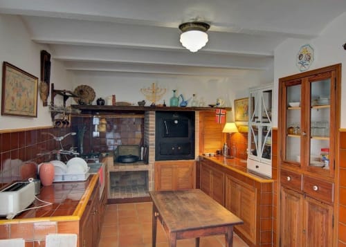 Rustic kitchen at Casa Gallinera in Benissivà with wooden cabinetry, terracotta tiles, and traditional stove