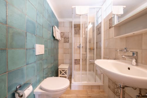 Salle de bain moderne à l'Appartement Supérieur de la Residenza Motta à Locarno, avec carrelage turquoise, douche à l'italienne et sanitaires blancs