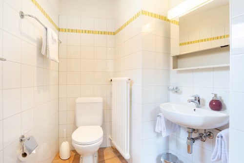 Salle de bain moderne aux carreaux blancs, bordures jaunes, lavabo, toilettes et radiateur à la Residenza Motta B&B à Locarno