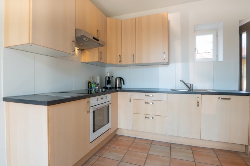 Cuisine moderne de l'appartement Residenza Motta avec meubles en bois clair, plan de travail sombre et carrelage terracotta