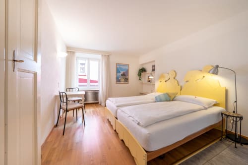 Camera luminosa presso la Residenza Motta a Locarno con letti gemelli, testata gialla, pavimenti in legno e vista sul giardino