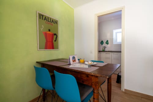 Coin cuisine lumineux à la Residenza Motta Locarno avec mur vert citron, affiche de café italienne, chaises turquoise, table en bois