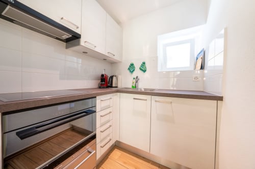 Cuisine moderne de l'appartement Residenza Motta à Locarno, avec meubles blancs, plan de travail foncé et four inox