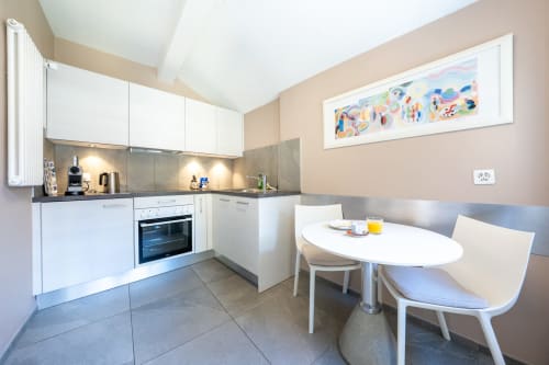 Cuisine et salle à manger modernes de l'appartement Residenza Motta avec placards blancs, carrelage gris et table ovale à Locarno