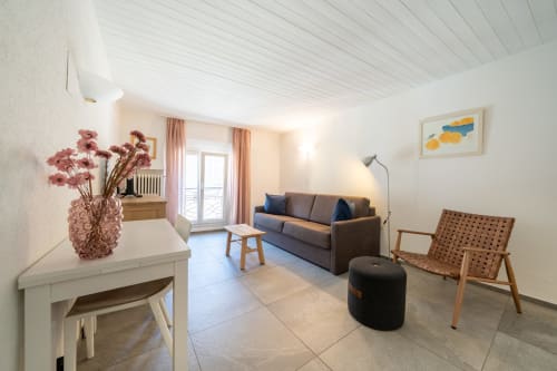 Salon lumineux du studio 2-pièces à Residenza Motta, Locarno avec canapé, fauteuil, fleurs et vue sur le jardin
