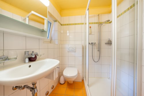 Salle de bain moderne à la Residenza Motta, Locarno avec carrelage blanc, sol orange, lavabo, toilettes et douche