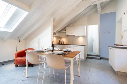 Cuisine et salle à manger modernes au dernier étage de Locarno avec puits de lumière, armoires blanches, table en bois et accents orange