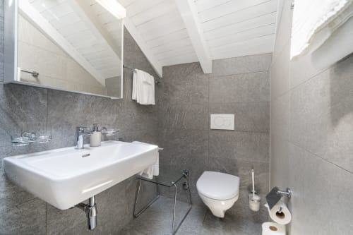 Salle de bain moderne à la Residenza Motta Locarno avec lavabo blanc, toilettes murales, carrelage gris et plafond avec puits de lumière