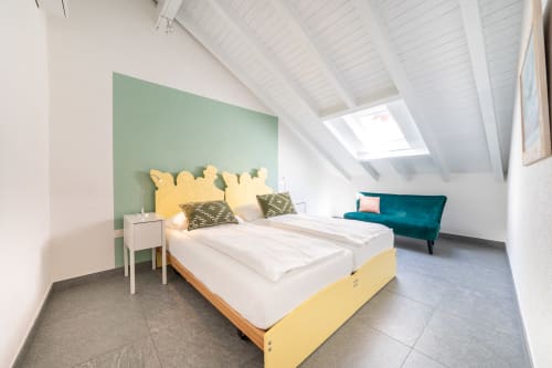 Camera da letto sottotetto luminosa presso Residenza Motta con letto giallo, parete color verde salvia, lucernari, divano teal e arredamento minimalista