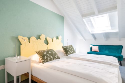 Chambre mansardée lumineuse à la Residenza Motta Locarno avec murs menthe, tête de lit jaune, literie blanche et canapé turquoise sous lucarne