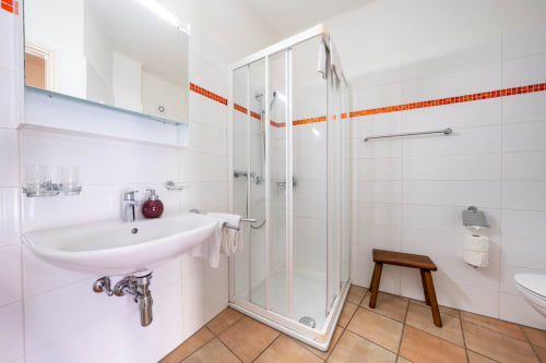 Salle de bains moderne du Studio N° 7 à la Residenza Motta, Locarno, avec carrelage blanc, accents orange, douche vitrée et