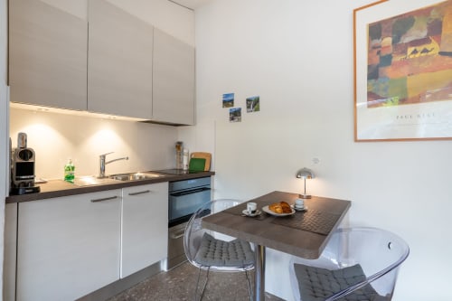 Cuisine et salle à manger modernes à la Residenza Motta à Locarno avec armoires blanches, plans de travail foncés et table de repas