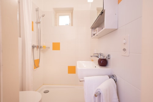 Salle de bain moderne avec douche, lavabo et équipements blancs avec touches jaunes à la Residenza Motta B&B, Locarno
