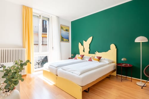 Monolocale accogliente alla Residenza Motta, Locarno con letto giallo, parete verde, pavimento in legno e vista sulla città