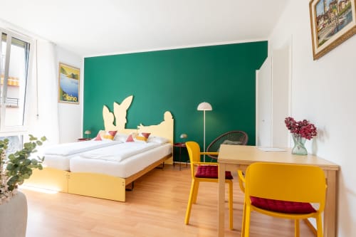 Studio cosy à la Residenza Motta à Locarno avec mur bleu-vert, lit jaune, table à manger et mobilier moderne