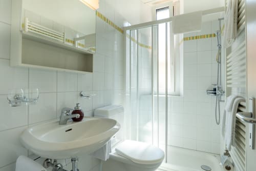 Salle de bain moderne à la Residenza Motta à Locarno avec carrelage blanc, lavabo, toilettes, cabine de douche et sèche-serviettes chauffant
