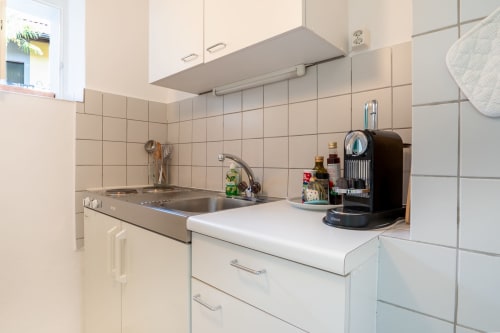 Kitchenette moderne à l'appartement studio Residenza Motta à Locarno, avec évier, plaque de cuisson, comptoirs blancs et dosseret en carrelage