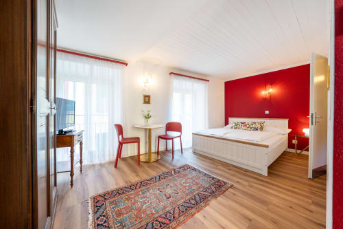 Camera moderna presso la Residenza Motta Locarno con parete rossa di accento, letto bianco e balcone con vista sulla città
