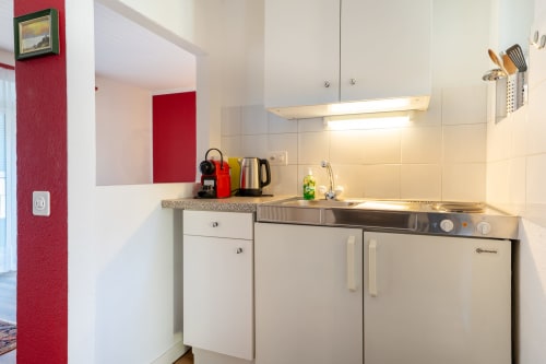 Cuisine contemporaine à l'appartement Residenza Motta avec armoires blanches, appareils inox et mur d'accent rouge à Locarno