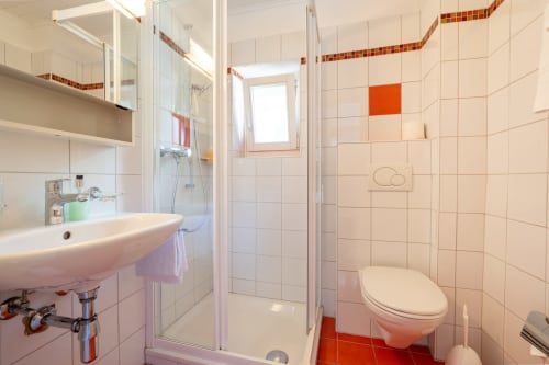 Salle de bain moderne de la Chambre 15 à la Residenza Motta Locarno avec douche, lavabo, WC et accents de carrelage orange