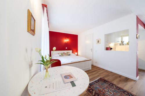 Chambre moderne à la Residenza Motta Locarno avec mur d'accent rouge, lit blanc, table ronde avec fleurs et salle de bain attenante
