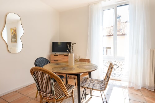Salle à manger ensoleillée à la Residenza Motta avec table ronde, chaises tressées, télévision et vue sur la ville par les portes vitrées