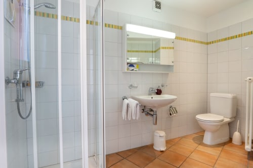 Salle de bain moderne de l'appartement Residenza Motta à Locarno, avec carrelage blanc, douche, lavabo, toilettes et sol en terre cuite