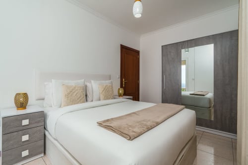 Modern bedroom with white bed, gray nightstand, and ensuite bathroom at Garry's Holiday Rentals in Arco da Calheta, Portugal