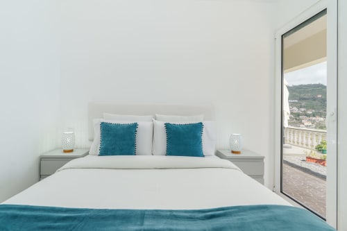 Modern bedroom with teal pillows, white bedding, sea view balcony overlooking Arco da Calheta, Portugal at Garry's Holiday