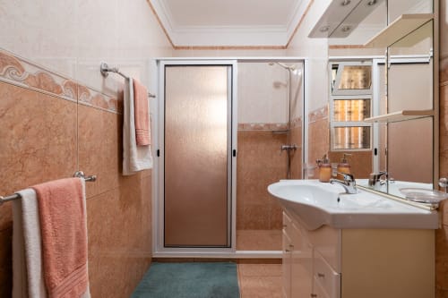 Modern bathroom with coral tile walls, white sink, mirror, and shower in Azul Infinito Casa apartment, Arco da Calheta