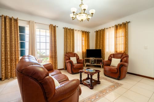 Spacious living room with brown leather armchairs, TV, and gold curtains in Azul Infinito Casa apartment at Garry's Holiday