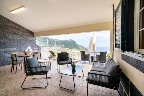 Modern terrace with sea view, outdoor seating, and coastal mountain landscape at Azul Infinito Casa in Arco da Calheta,