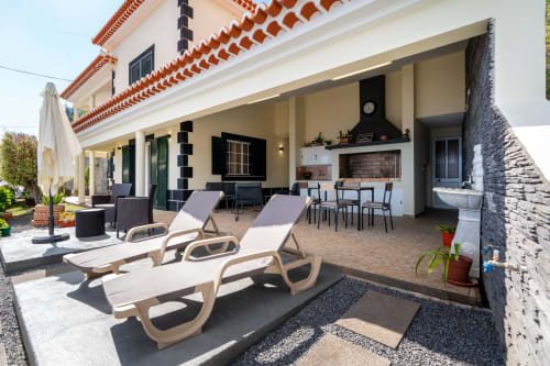 Azul Infinito Casa 2BR terrace with sun loungers, outdoor furniture, and fireplace in Arco da Calheta, Portugal