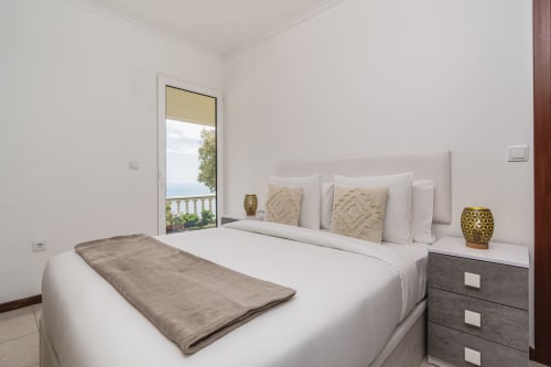Modern bedroom at Azul Infinito Casa with sea view, white bedding, neutral décor, and balcony access in Arco da Calheta,