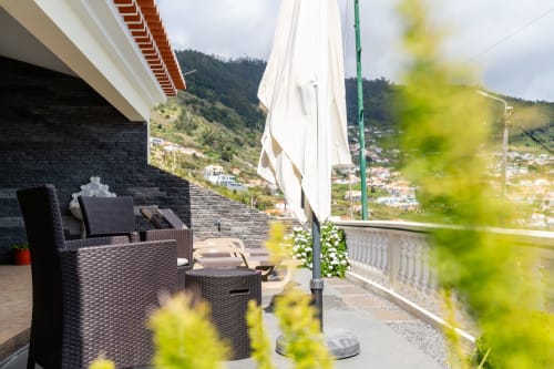 Terrace with rattan furniture, white umbrella, and mountain views at Azul Infinito Casa in Arco da Calheta, Portugal