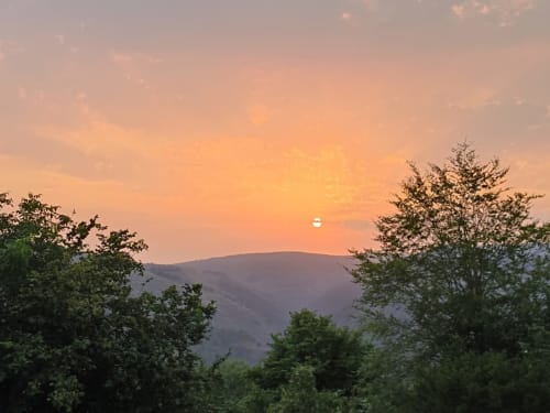 Sunset over mountains near Posada La Colodra hotel in Spain, with green trees framing the view