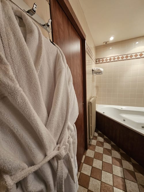 Salle de bain luxueuse avec baignoire balnéo, carrelage beige, accents marrons et serviettes moelleuses à l'Hôtel La Route d'Argent, Bozouls
