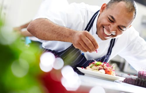 Chef en train de dresser un plat coloré à l'hôtel Anne Duval à Saint-Florent, souriant en garnissant avec des légumes
