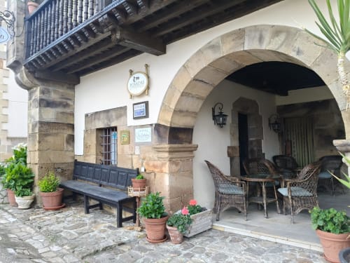 Posada La Colodra entrance with stone arch, potted flowers, wooden chairs, and bench seating in Spain