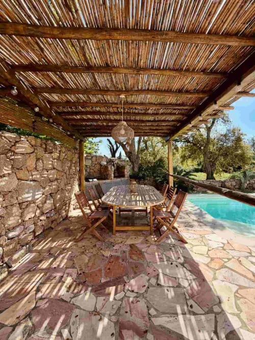 Espace repas ombragé à la pergola de la Villa Noti à Porto-Vecchio avec table en bois, chaises et vue sur la piscine privée turquoise