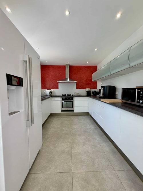 Cuisine moderne avec armoires blanches, mur d'accent rouge, comptoirs noirs et appareils en acier inoxydable à Villa Noti