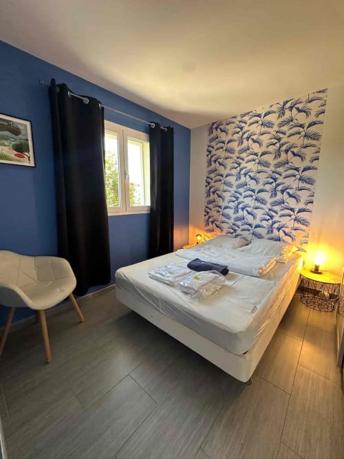 Chambre moderne aux Villas d'A Storia : murs bleus, lit blanc, tête de lit à motifs de palmiers, éclairage chaleureux